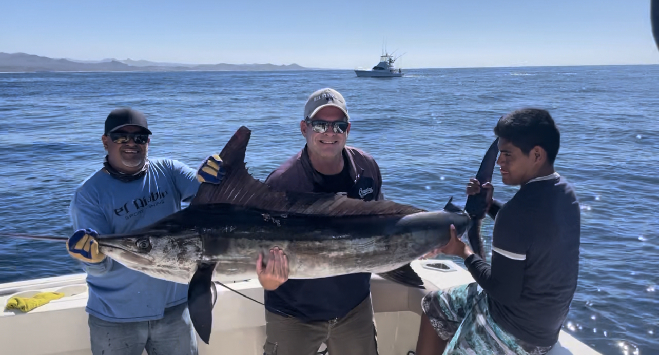 Cabo fishing crew and angler holding a striped marlin beside the boat