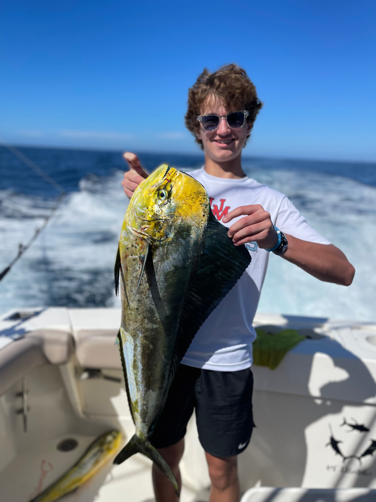 Young angler holding a vividly colored dorado aboard a Cabo sportfishing boat