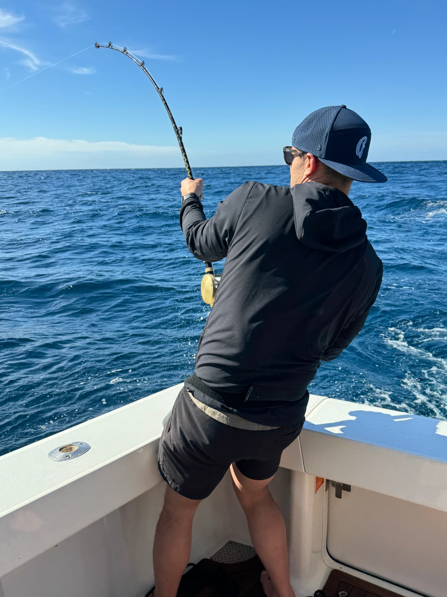 Angler fighting a fish with a bent rod aboard a Cabo charter boat